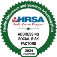 A circular green badge with the text Health Resources and Services Administration around the edge. Center text reads HRSA Health Center Program, Addressing Social Risk Factors, 2024 Awardee—recognizing Montrose Health Care’s commitment to quality healthcare.