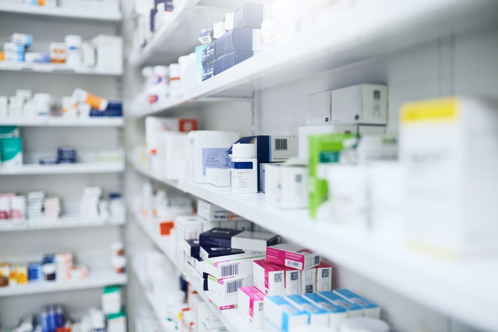 Shelves filled with various boxes and packages of medications in a pharmacy, organized in rows with different colors and labels visible, highlight the commitment to affordable health care at Grand Junction Health Care.