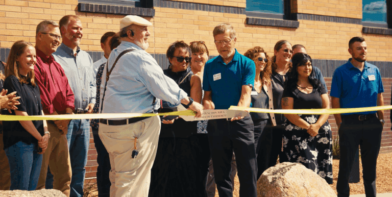 two men hold a ribbon while a woman with giant scissors cuts the ribbon while a group of people look on at primehealth plus health clinic in grand junction