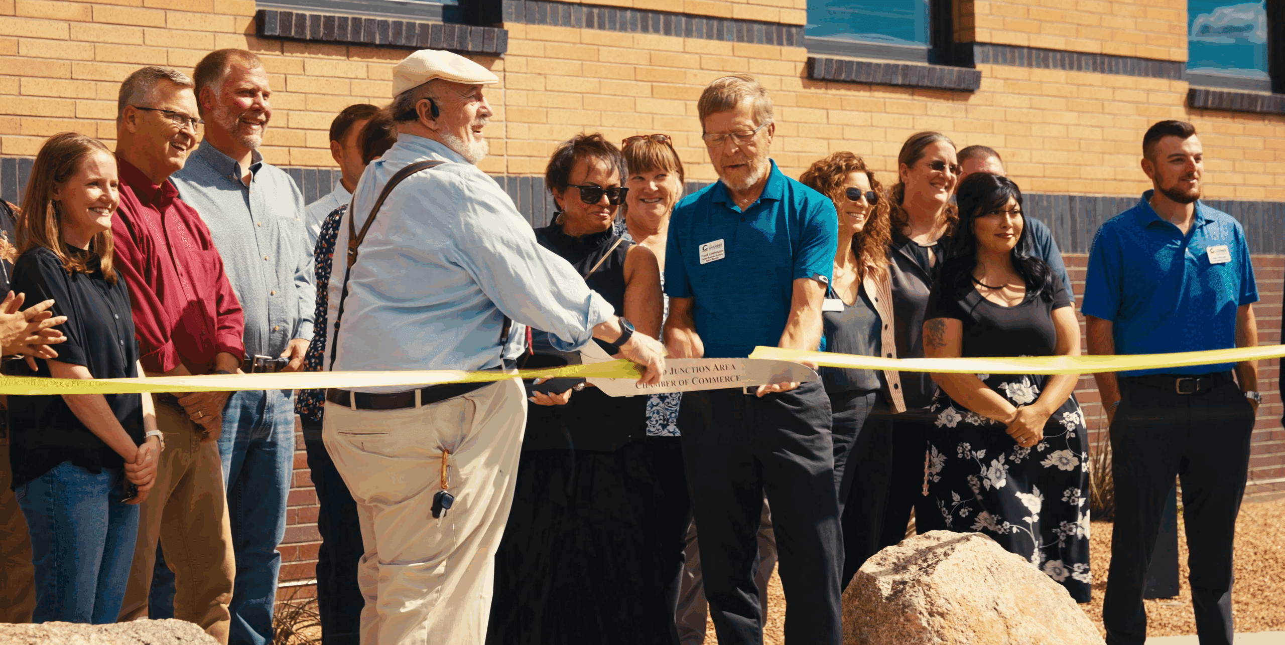 two men hold a ribbon while a woman with giant scissors cuts the ribbon while a group of people look on at primehealth plus health clinic in grand junction